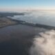 alt="Fotografía aérea de la represa de Salto Grande rodeada de nubes bajas y neblina, ilustrando la preparación frente a El Niño en Salto Grande"